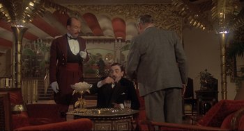 Movie still from “Murder on the Orient Express” (1974), directed by Sidney Lumet – A man in a suit is sitting at a coffee table; Wide shot, Low angle