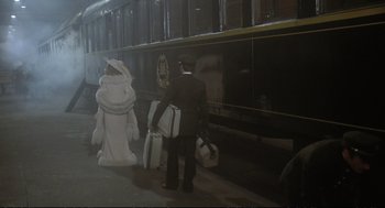 Movie still from “Murder on the Orient Express” (1974), directed by Sidney Lumet – A man in a suit and hat with suitcases next to a train; Wide shot, Over the shoulder angle