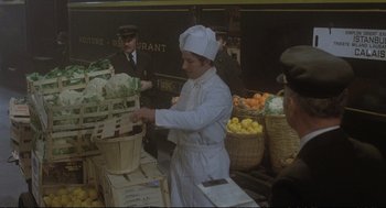 Movie still from “Murder on the Orient Express” (1974), directed by Sidney Lumet – A man wearing a chef's hat standing in front of baskets filled with fruit; Medium shot, High angle