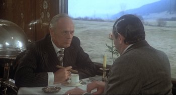 Movie still from “Murder on the Orient Express” (1974), directed by Sidney Lumet – Two men sitting at a table with a cup of coffee; Medium shot, Over the shoulder angle