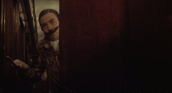 Movie still from “Murder on the Orient Express” (1974), directed by Sidney Lumet – A man with a fake mustache standing next to a door; Medium shot, Over the shoulder angle