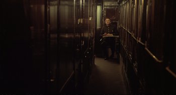 Movie still from “Murder on the Orient Express” (1974), directed by Sidney Lumet – A man sitting on a chair inside of a room; Wide shot, High angle
