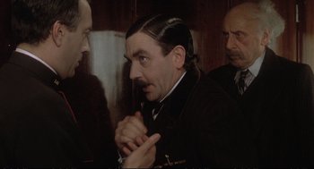 Movie still from “Murder on the Orient Express” (1974), directed by Sidney Lumet – A man in a suit and tie talking to two other men; Close Up shot, Over the shoulder angle
