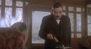 Movie still from “Murder on the Orient Express” (1974), directed by Sidney Lumet – A man in a suit and tie holding a bottle of wine; Medium shot, Low angle