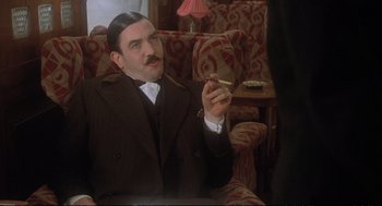 Movie still from “Murder on the Orient Express” (1974), directed by Sidney Lumet – A man sitting in a chair holding a cigarette in his hand; Medium shot, Low angle