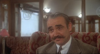 Movie still from “Murder on the Orient Express” (1974), directed by Sidney Lumet – An older man with a mustache sitting on a couch; Close Up shot, Over the shoulder angle