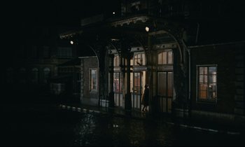 Movie still from “Muriel” (1963), directed by Alain Resnais – A person walking in front of a building at night; Extreme Wide shot, High angle