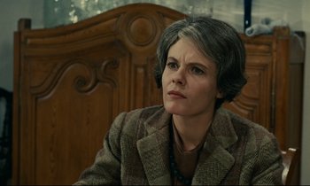 Movie still from “Muriel” (1963), directed by Alain Resnais – An older woman sitting in a chair looking at the camera; Close Up shot, Low angle