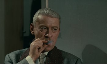 Movie still from “Muriel” (1963), directed by Alain Resnais – An older man smoking a cigarette while wearing a suit and tie; Close Up shot, Low angle