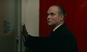Movie still from “Muriel” (1963), directed by Alain Resnais – A man standing in front of a red door; Close Up shot, Over the shoulder angle