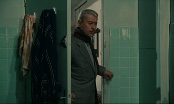 Movie still from “Muriel” (1963), directed by Alain Resnais – A man standing in front of a bathroom door; Medium shot, Over the shoulder angle