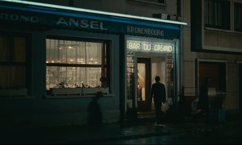 Movie still from “Muriel” (1963), directed by Alain Resnais – A man walking down the street in front of a building; Wide shot, Over the shoulder angle