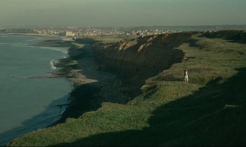 Movie still from “Muriel” (1963), directed by Alain Resnais – A person standing on top of a hill near the ocean; Extreme Wide shot, High angle