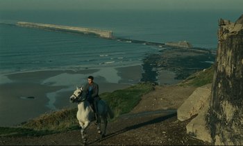 Movie still from “Muriel” (1963), directed by Alain Resnais – A man riding a white horse down a hill near the ocean; Extreme Wide shot, High angle