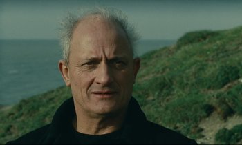 Movie still from “Muriel” (1963), directed by Alain Resnais – An older man with a white beard is standing on a hill; Close Up shot, Low angle