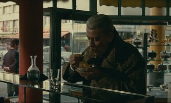 Movie still from “Muriel” (1963), directed by Alain Resnais – An older man eating a bowl of food at a restaurant; Medium shot, Over the shoulder angle