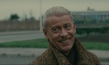 Movie still from “Muriel” (1963), directed by Alain Resnais – An older man with white hair smiling for the camera; Close Up shot, Over the shoulder angle