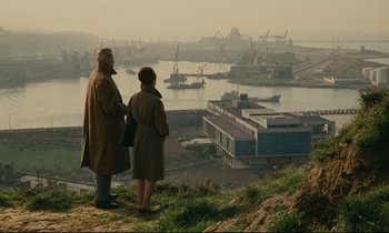 Movie still from “Muriel” (1963), directed by Alain Resnais – A man and a woman standing on top of a hill looking at a harbor; Extreme Wide shot, High angle