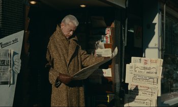 Movie still from “Muriel” (1963), directed by Alain Resnais – An older man reading a newspaper in front of a store window; Medium shot, Low angle