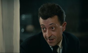 Movie still from “Muriel” (1963), directed by Alain Resnais – A person wearing a suit and tie; Close Up shot, High angle