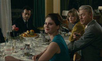 Movie still from “Muriel” (1963), directed by Alain Resnais – A group of people sitting at a table with plates of food on it; Medium shot, Over the shoulder angle
