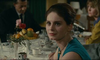 Movie still from “Muriel” (1963), directed by Alain Resnais – A woman sitting at a dinner table looking at the camera; Close Up shot, Over the shoulder angle