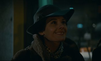 Movie still from “Muriel” (1963), directed by Alain Resnais – A woman wearing a black hat and a scarf smiling; Close Up shot, Low angle