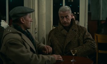 Movie still from “Muriel” (1963), directed by Alain Resnais – Two older men sitting at a table with a glass of wine; Medium shot, Over the shoulder angle