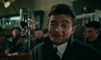 Movie still from “Muriel” (1963), directed by Alain Resnais – A person wearing a suit and tie; Close Up shot, Over the shoulder angle