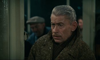 Movie still from “Muriel” (1963), directed by Alain Resnais – An older man in a brown coat is looking at the camera; Close Up shot, High angle