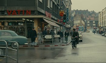 Movie still from “Muriel” (1963), directed by Alain Resnais – A man riding a bike down a street next to a building; Extreme Wide shot, High angle
