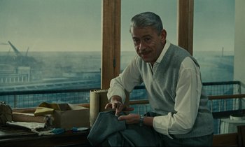 Movie still from “Muriel” (1963), directed by Alain Resnais – An older man sitting in front of a window; Medium shot, Over the shoulder angle