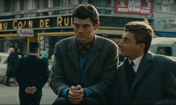 Movie still from “Muriel” (1963), directed by Alain Resnais – A man in a suit sitting next to another man in a suit; Medium shot, Over the shoulder angle