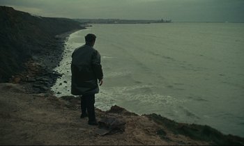 Movie still from “Muriel” (1963), directed by Alain Resnais – A man standing on top of a cliff looking out at the ocean; Extreme Wide shot, High angle