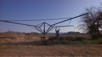 Movie still from “Murphy's Romance” (1985), directed by Martin Ritt – A man standing next to a metal structure in a field; Extreme Wide shot, Low angle