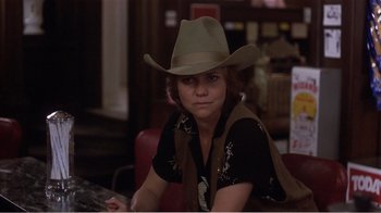 Movie still from “Murphy's Romance” (1985), directed by Martin Ritt – A woman wearing a cowboy hat sitting at a table; Close Up shot, Over the shoulder angle