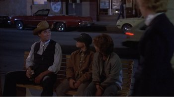 Movie still from “Murphy's Romance” (1985), directed by Martin Ritt – A group of people sitting on top of a wooden bench; Medium shot, Over the shoulder angle