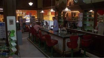 Movie still from “Murphy's Romance” (1985), directed by Martin Ritt – A man standing at a counter in front of a bar; Wide shot, High angle