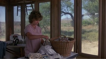Movie still from “Murphy's Romance” (1985), directed by Martin Ritt – A woman holding a bag near a basket of laundry; Medium shot, Over the shoulder angle