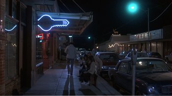 Movie still from “Murphy's Romance” (1985), directed by Martin Ritt – A group of people sitting on a sidewalk at night; Wide shot, High angle