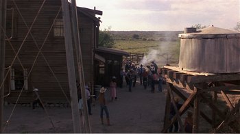 Movie still from “Murphy's Romance” (1985), directed by Martin Ritt – A group of people standing outside of a wooden building; Extreme Wide shot, Over the shoulder angle
