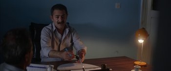 Movie still from “Mustang” (2015), directed by Deniz Gamze Ergüven – A man sitting at a table cutting paper with a pair of scissors; Medium shot, High angle