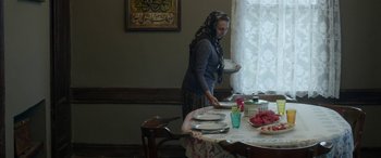 Movie still from “Mustang” (2015), directed by Deniz Gamze Ergüven – A woman standing at a dining room table holding a plate; Wide shot, Over the shoulder angle