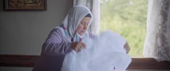 Movie still from “Mustang” (2015), directed by Deniz Gamze Ergüven – An older woman in a headscarf is sewing a white cloth; Medium shot, Low angle