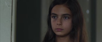 Movie still from “Mustang” (2015), directed by Deniz Gamze Ergüven – A young girl with long dark hair and blue eyes looking at the camera; Close Up shot, Over the shoulder angle