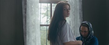 Movie still from “Mustang” (2015), directed by Deniz Gamze Ergüven – A young woman with long hair standing in front of a window; Medium shot, Over the shoulder angle