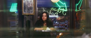 Movie still from “My Blueberry Nights” (2007), directed by Kar-Wai Wong – A woman sitting at a table in front of a neon sign; Medium shot, Over the shoulder angle