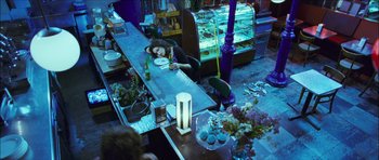 Movie still from “My Blueberry Nights” (2007), directed by Kar-Wai Wong – A woman sitting at a table with a plate in front of her face; Wide shot, Overhead angle
