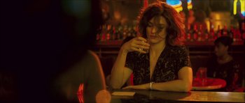 Movie still from “My Blueberry Nights” (2007), directed by Kar-Wai Wong – A woman sitting at a table in front of a glass of wine; Medium shot, Over the shoulder angle
