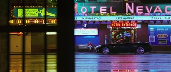Movie still from “My Blueberry Nights” (2007), directed by Kar-Wai Wong – A man sitting on a bench in front of a neon sign; Wide shot, High angle